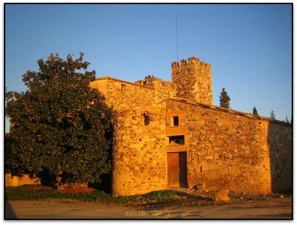 Fachada de piedra de una masía con torre iluminada por el sol de la tarde