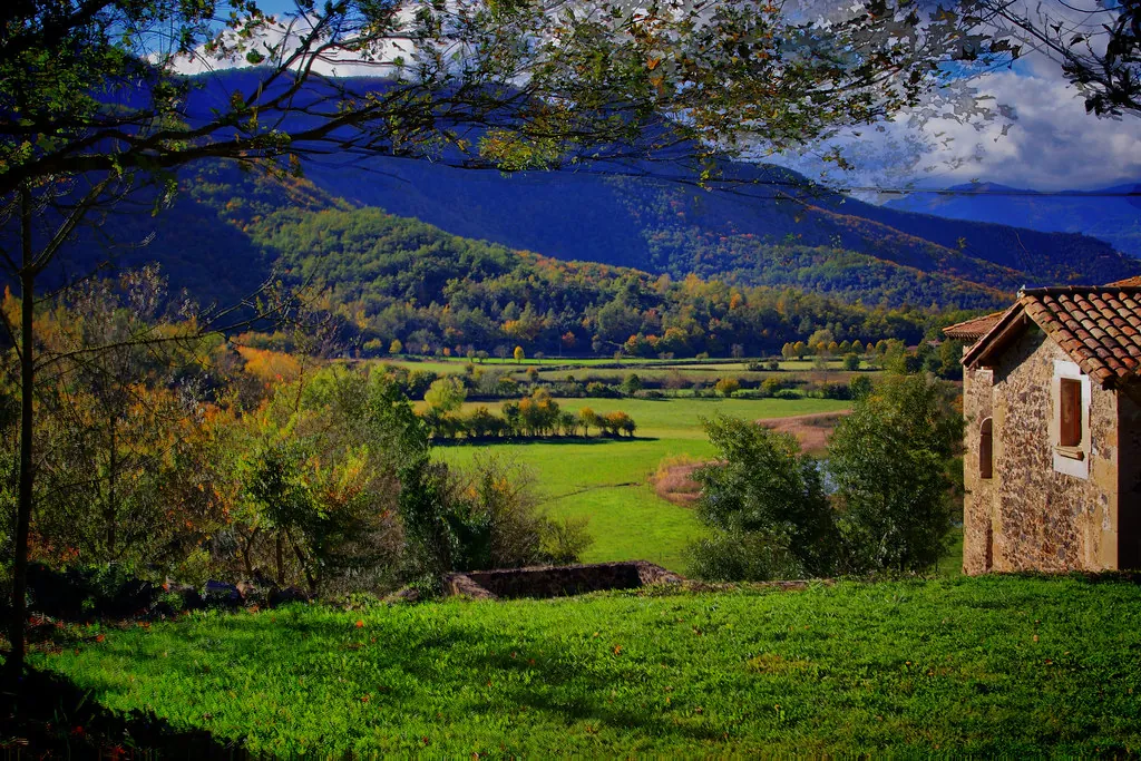 Valle verde de la Garrotxa con montañas azules y una casa de piedra entre los árboles